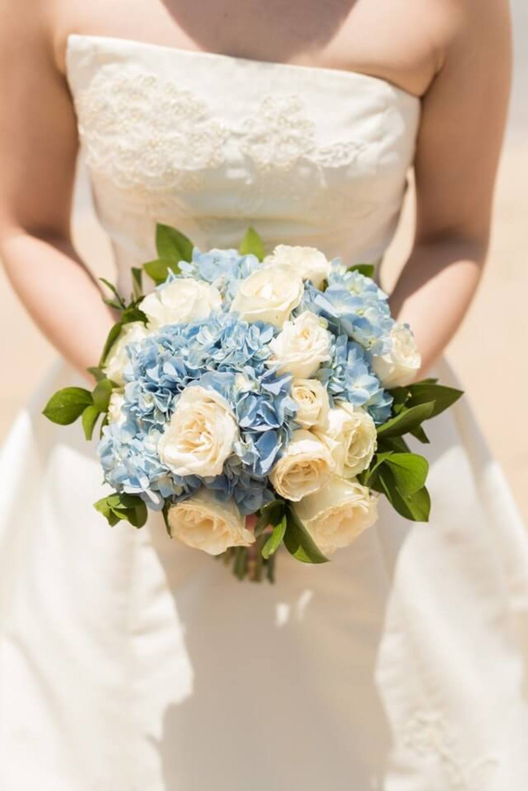 Kytica z modrých hortenzií a krémových ruží v rukách nevesty